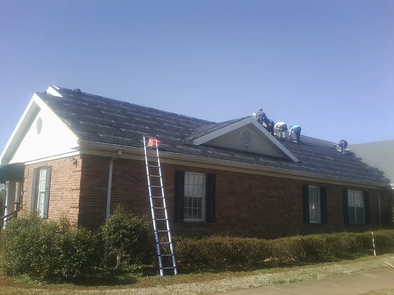 Crew tearing shingles off a brick ranch roof with a ladder set — Metal Roof Repair work by our crew in Filer