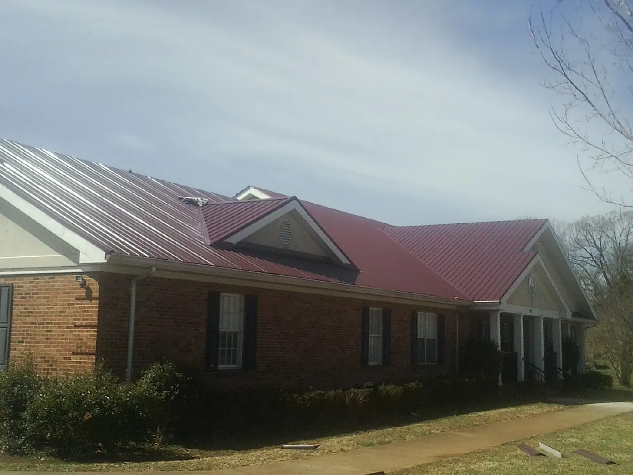 Red metal roof with gabled entries on a long brick building, from a Hail Damage Roof Repair job in Filer