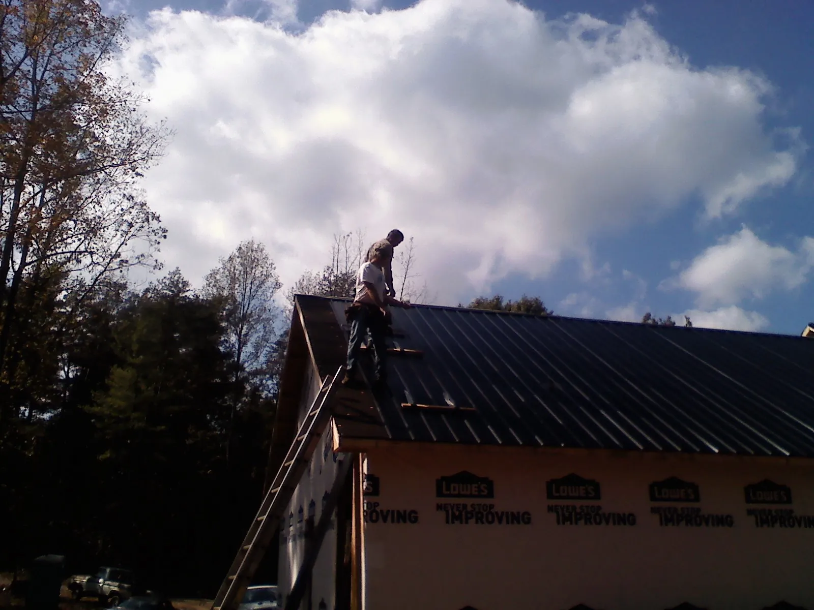 Roofer fastening dark metal panels high against a cloudy sky, from a Roof Inspection job in Filer